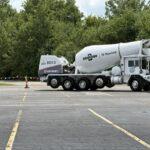 White Oshkosh S-Series concrete mixer truck parked in an empty parking lot with trees in the background.