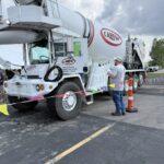 White CAREW cement mixer truck parked in a lot, with a man in a cap inspecting near the side behind safety barriers.