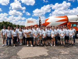 Group of workers in gray shirts with lanyards posing in front of a Peters Concrete cement mixer truck on a sunny day.